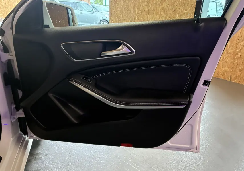 Porte avant gauche ouverte d'une Mercedes Classe A 200D blanche, montrant le panneau intérieur noir avec surpiqûres blanches.
