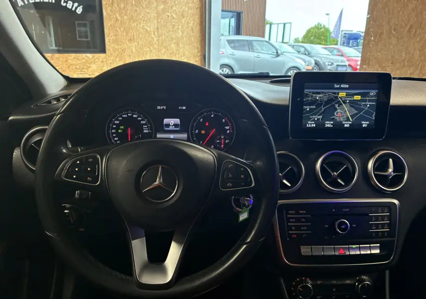 Vue intérieure centrée sur le volant noir Mercedes Classe A 2016 avec tableau de bord et écran GPS allumé.