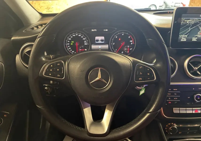 Vue centrée sur le volant cuir noir d'une Mercedes Classe A 200D 2016 avec tableau de bord et écran GPS allumé.