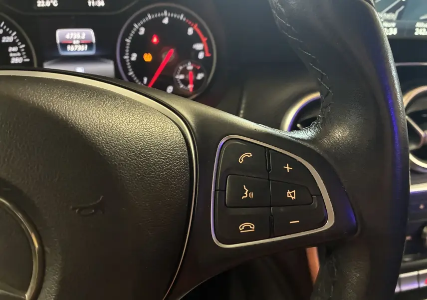 Gros plan sur le volant cuir noir de la Mercedes Classe A 200D 2016 avec commandes audio et tableau de bord éclairé.