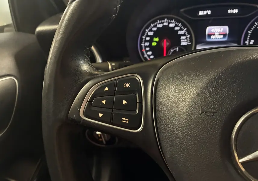 Gros plan sur le volant cuir noir de la Mercedes Classe A 200D 2016, avec commandes multifonctions et tableau de bord éclairé.