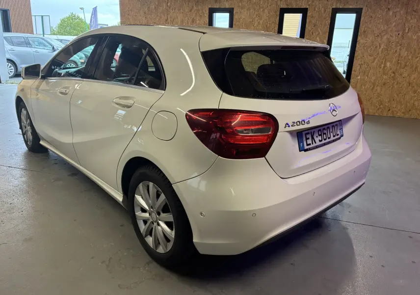 Vue 3/4 arrière droite d'une Mercedes Classe A 200D blanche, compacte avec feux arrière rouges et vitres teintées.