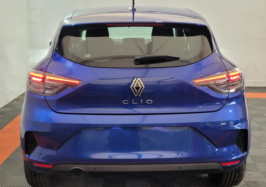 Vue arrière d'une Renault Clio bleu électrique avec feux arrière LED allumés dans un intérieur neutre.