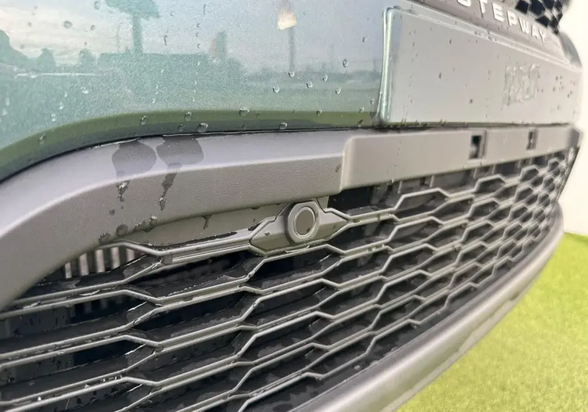Gros plan sur la calandre noire et le bouclier avant du Dacia Sandero III Stepway vert cèdre avec capteur de stationnement.