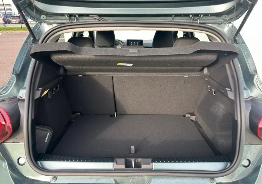 Coffre ouvert vu de l'arrière d'une Dacia Sandero III Stepway vert cèdre avec cache-bagages relevé.