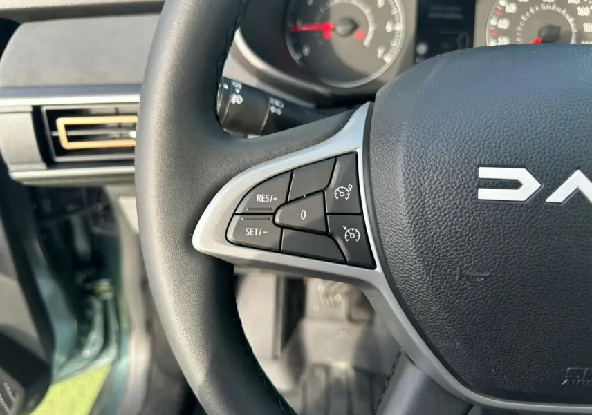 Gros plan sur le volant noir de la Dacia Sandero III Stepway avec commandes de régulateur de vitesse visibles.