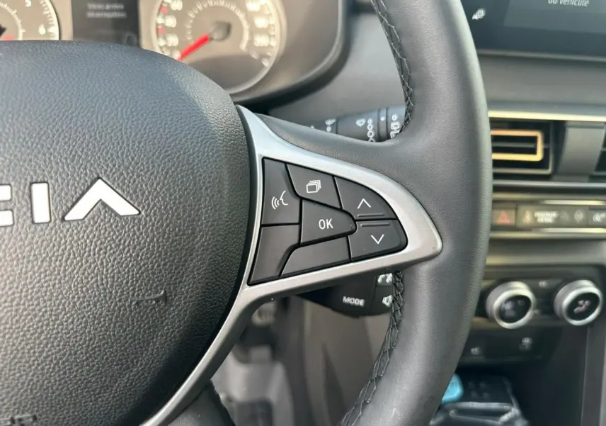 Gros plan sur le volant côté droit d’une Dacia Sandero III Stepway 2025, avec commandes intégrées et tableau de bord en arrière-plan.
