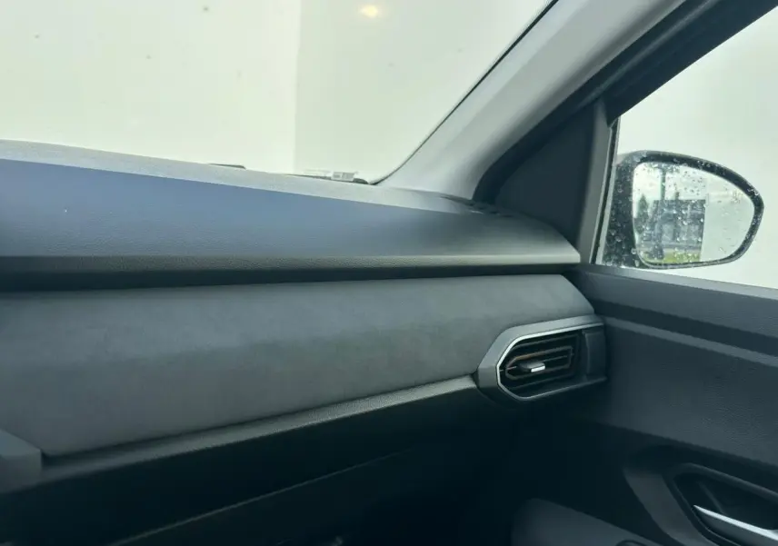 Vue intérieure côté passager avant de la Dacia Sandero III Stepway 2025, tableau de bord et aérateur noirs.