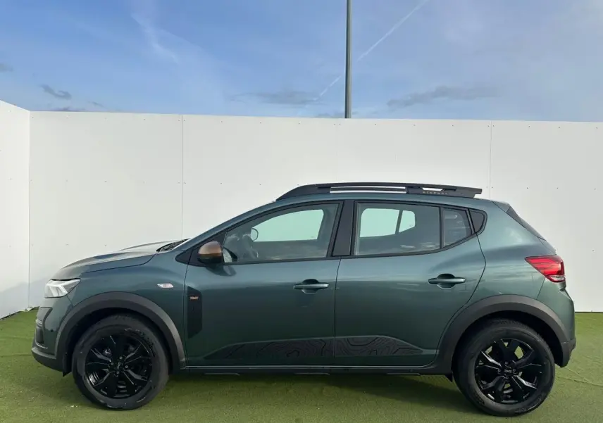 Vue latérale gauche d'une Dacia Sandero III Stepway vert cèdre avec jantes noires et barres de toit.