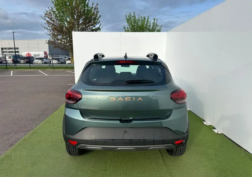 Vue arrière d'une Dacia Sandero III Stepway vert cèdre avec logo et lettrage brun cuivré, sur fond urbain.
