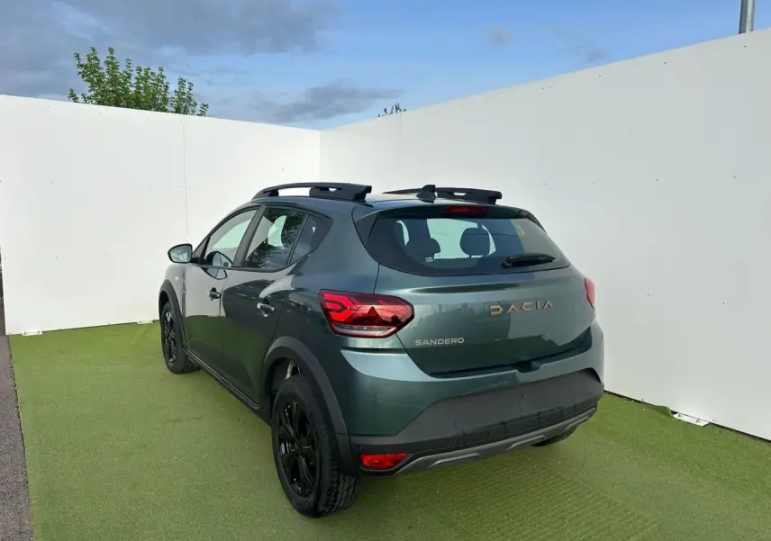 Vue 3/4 arrière droite d'une Dacia Sandero III Stepway vert cèdre avec barres de toit et jantes noires.