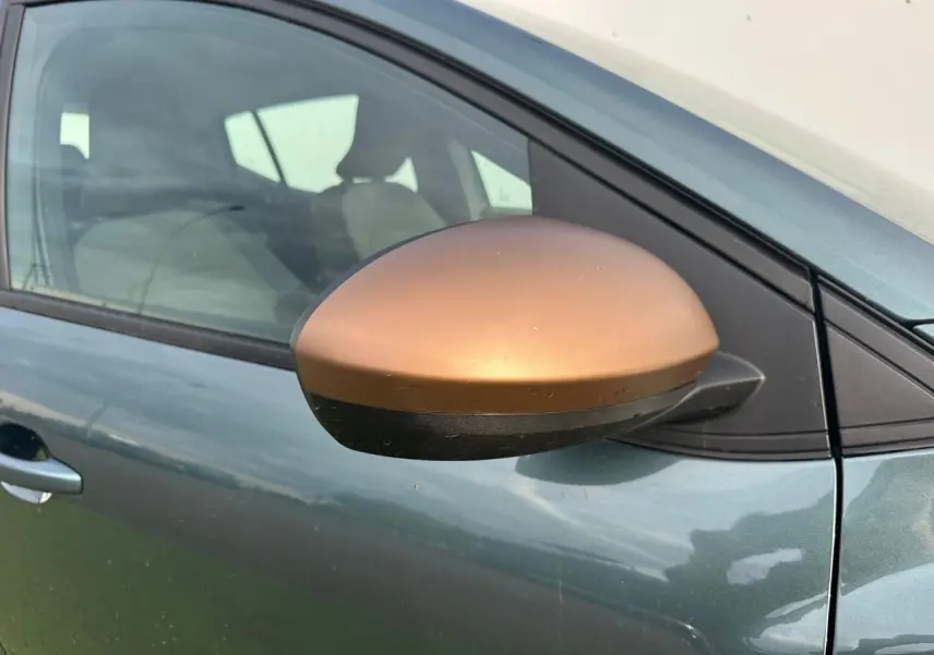 Gros plan sur le rétroviseur droit brun cuivré d'une Dacia Sandero III Stepway vert cèdre, côté conducteur visible.
