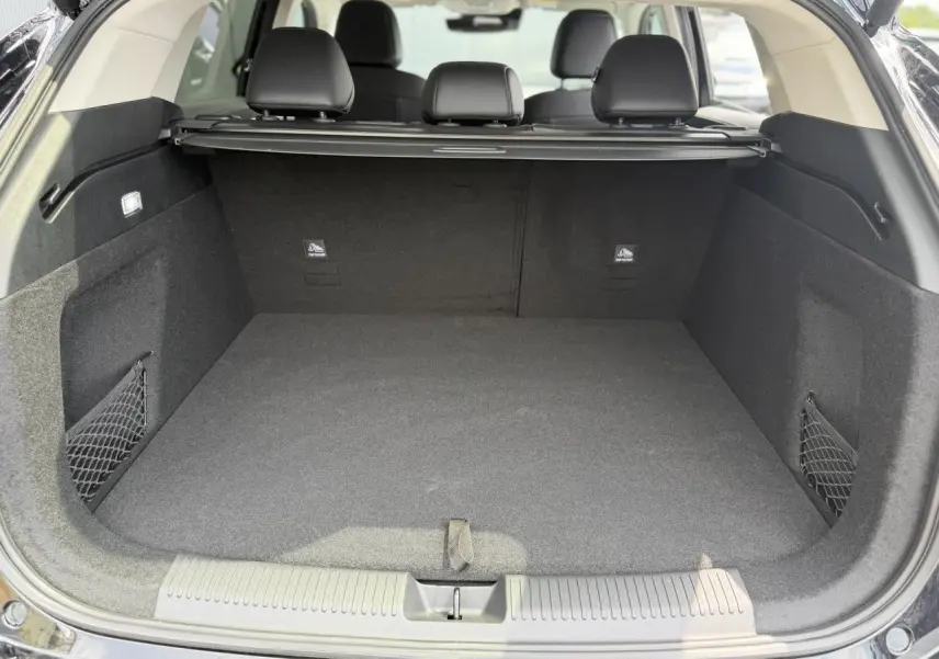 Coffre ouvert vu de l'arrière d'un MG Motor EHS noir, intérieur noir avec filet de rangement latéral.