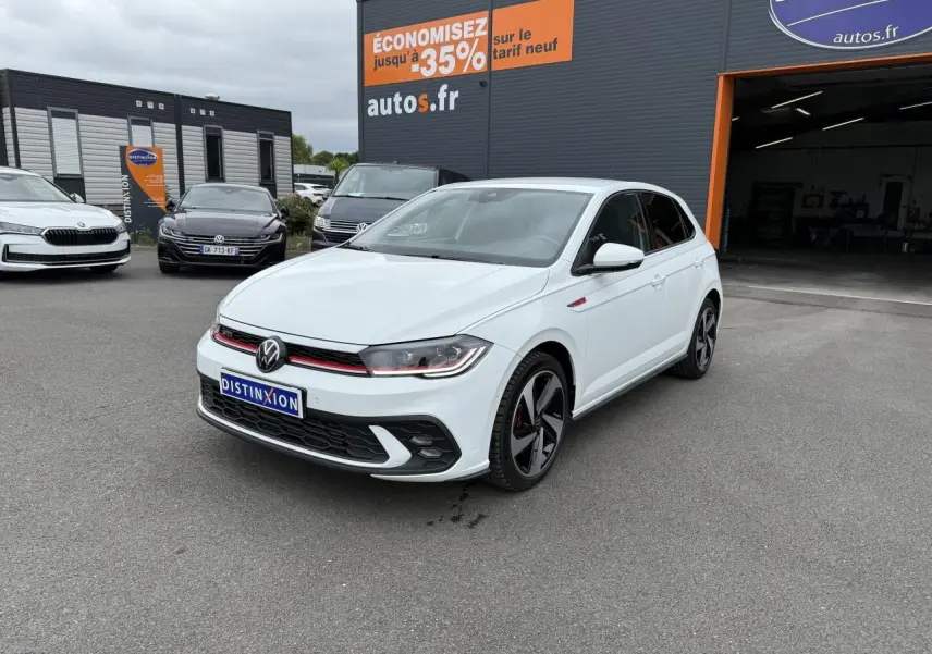 Volkswagen Polo GTI blanc pur vue 3/4 avant droit avec jantes noires et calandre rouge sur parking extérieur.