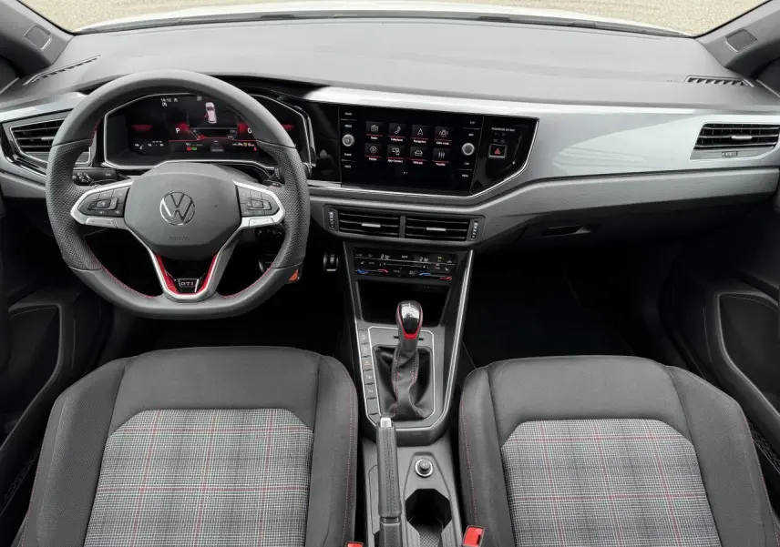 Vue intérieure avant de la Volkswagen Polo GTI 2024, tableau de bord moderne avec volant sport et sièges à motif tartan.
