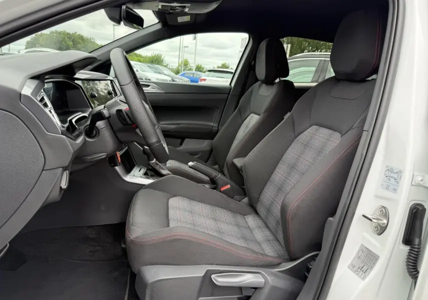 Intérieur avant droit d'une Volkswagen Polo blanche 2024, sièges tissu noir à motif écossais avec surpiqûres rouges.