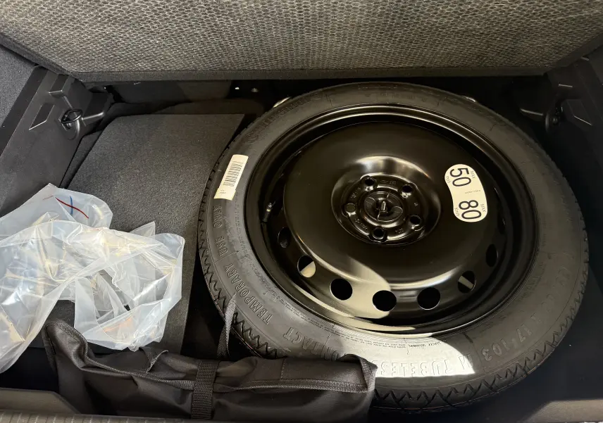Roue de secours compacte noire dans le coffre d'un Renault Captur gris Cassiopée Métal 2025, vue plongeante.
