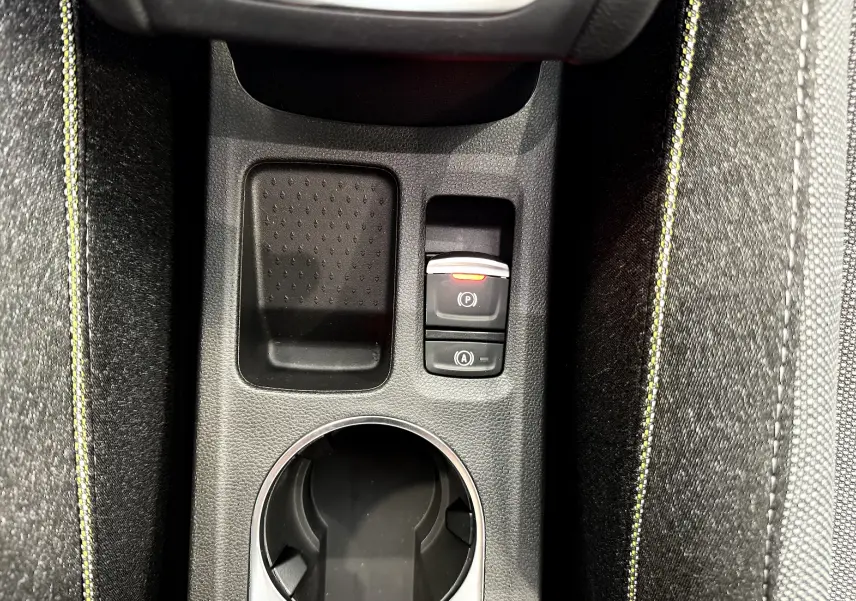 Gros plan sur la console centrale du Renault Captur gris, montrant le frein à main électrique et les surpiqûres jaunes des sièges.