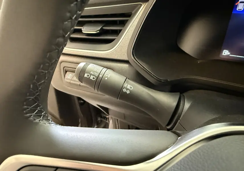 Détail du commodo d'éclairage à gauche du volant dans le Renault Captur gris Cassiopée 2025, version hybride.