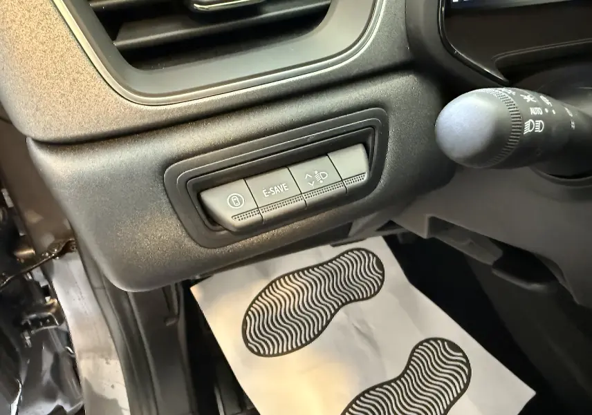 Gros plan sur les commandes E-SAVE et réglage des phares côté gauche du tableau de bord du Renault Captur gris Cassiopée 2025.