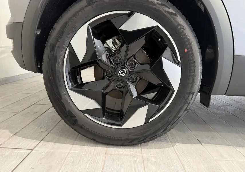 Gros plan sur la roue avant droite du Renault Captur gris Cassiopée, mettant en valeur la jante noire et argentée au design étoilé.
