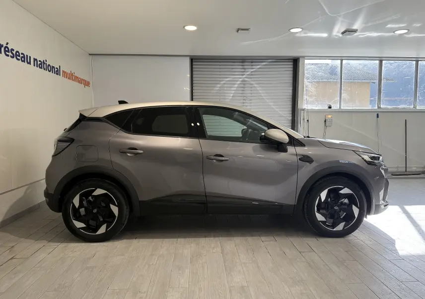 Profil droit d'un Renault Captur 2025 gris Cassiopée métal avec toit gris, roues noires et design moderne en intérieur showroom.