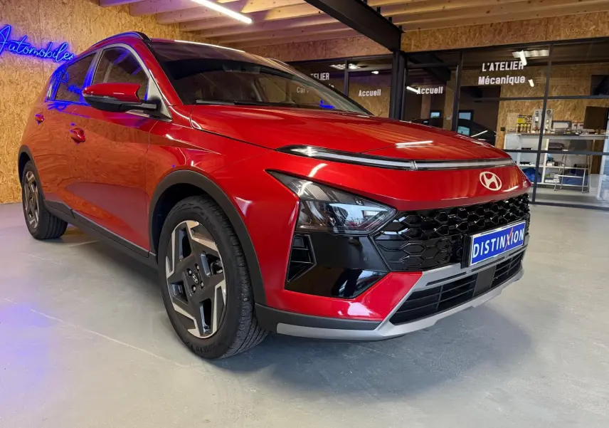 Vue 3/4 avant gauche d'une Hyundai Bayon rouge avec calandre noir laqué et jantes alu 17 pouces en intérieur showroom.