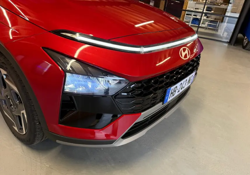 Gros plan sur l’avant droit du Hyundai Bayon rouge 2025 avec calandre noir laqué et feux LED distinctifs.