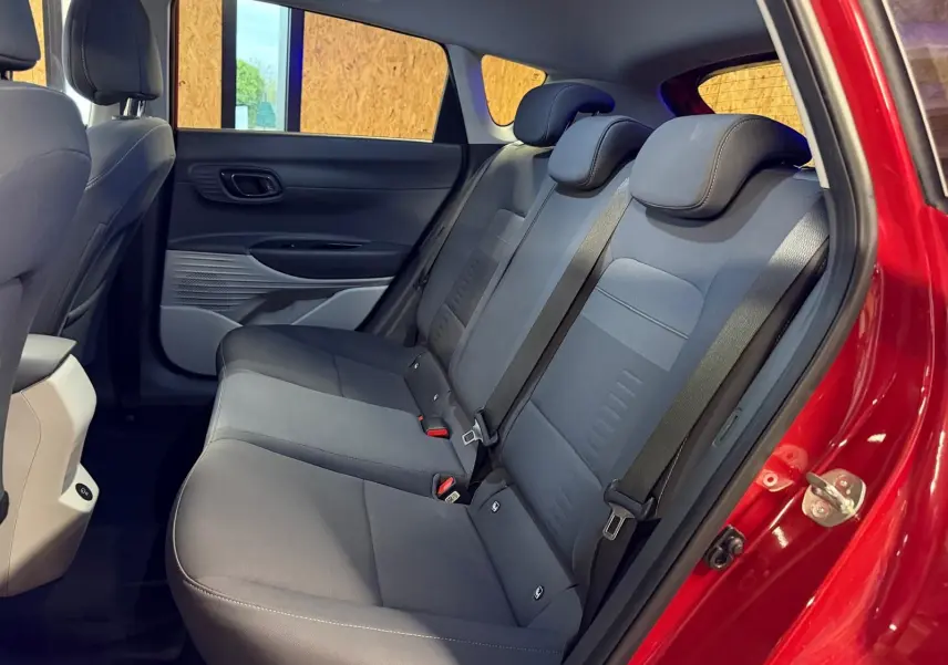 Vue intérieure côté droit sur la banquette arrière grise du Hyundai Bayon rouge avec ceinture de sécurité visible.