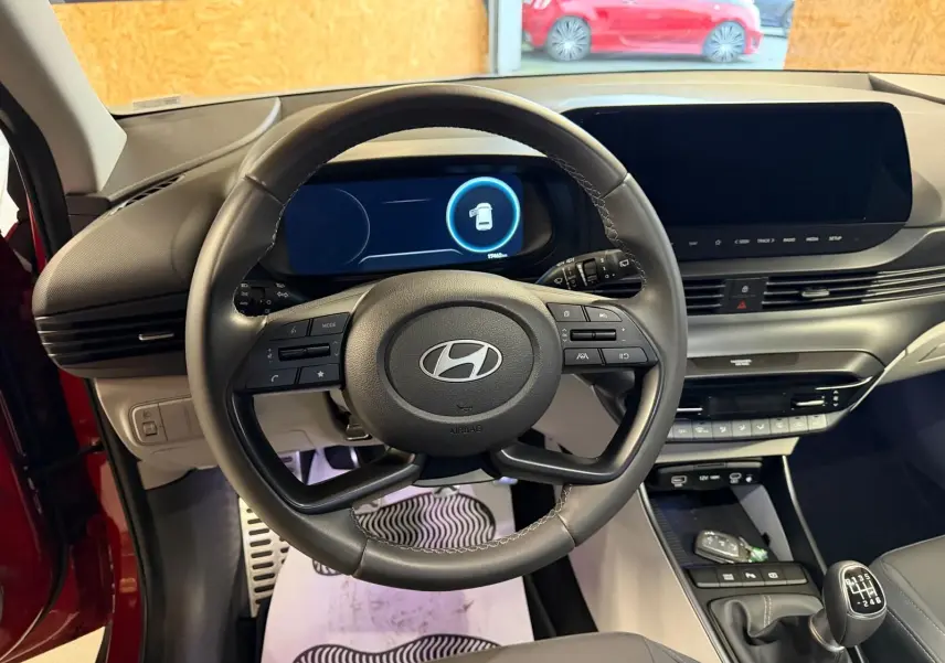 Vue intérieure centrée sur le volant cuir multifonctions et tableau de bord numérique du Hyundai Bayon rouge 2025.