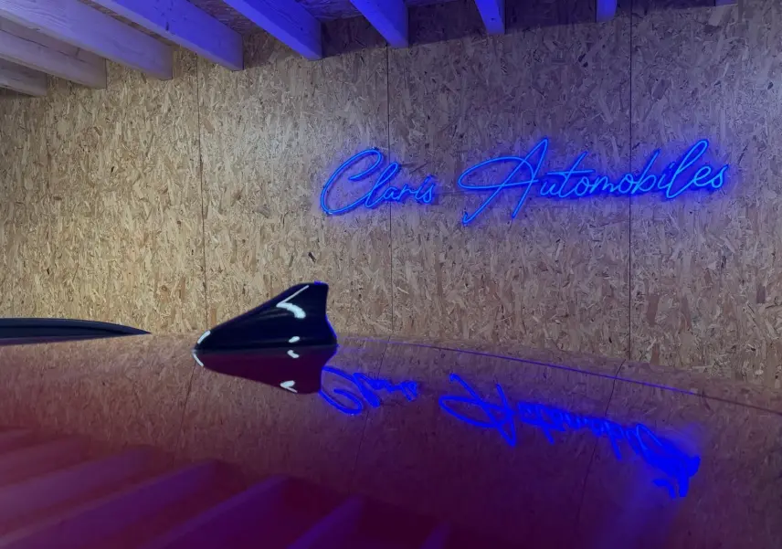 Antenne requin noire sur le toit d'une Hyundai Bayon rouge, reflet du néon bleu "Claris Automobiles" sur la carrosserie.