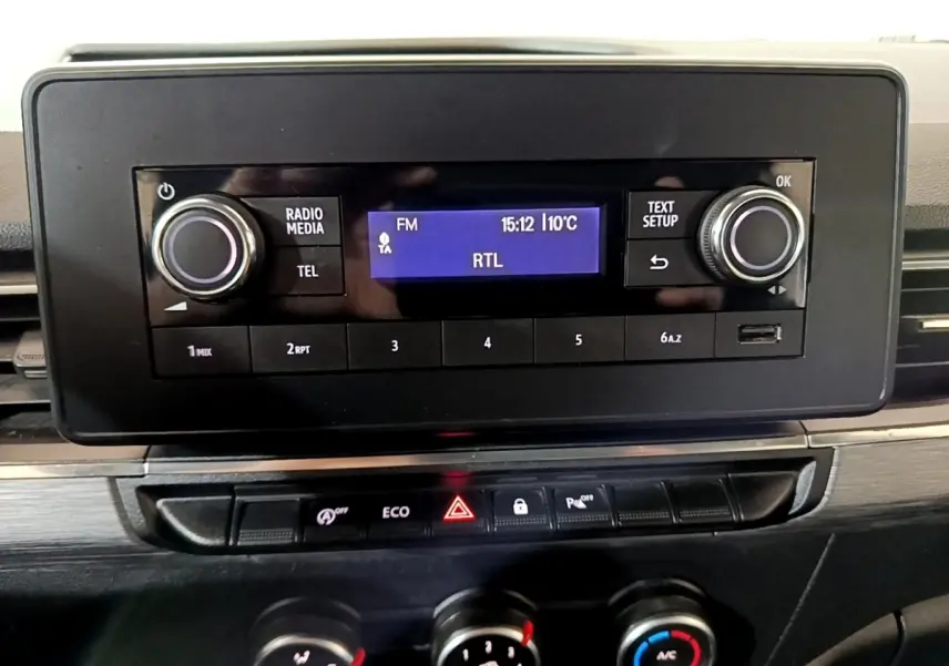 Gros plan sur le tableau de bord noir du Renault Kangoo blanc 2022, affichage radio FM et commandes climatisation visibles.