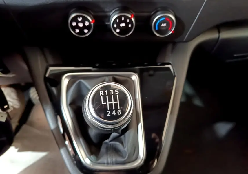 Gros plan sur le levier de vitesses manuel noir et chrome du Renault Kangoo blanc, avec commandes de climatisation en arrière-plan.