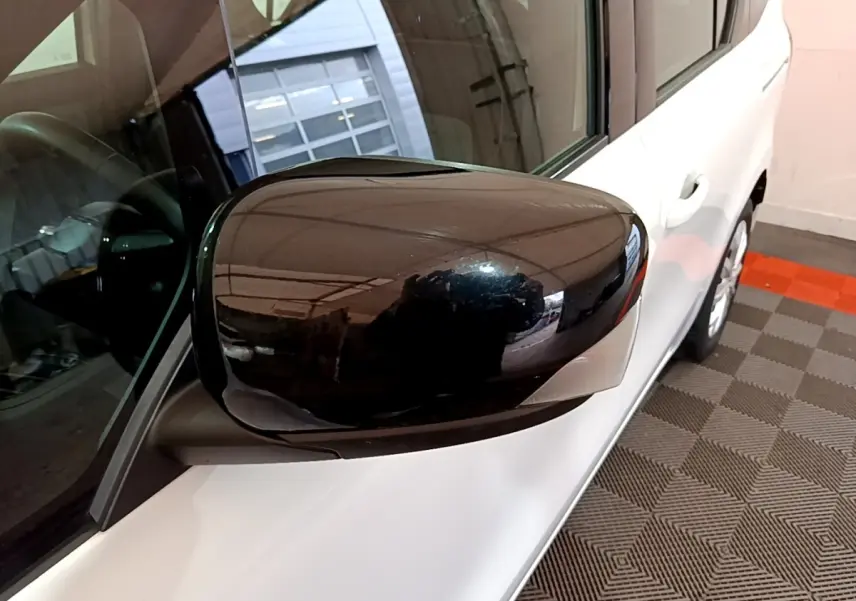 Gros plan sur le rétroviseur noir côté gauche d’un Renault Kangoo blanc, vue partielle du côté avant droit.