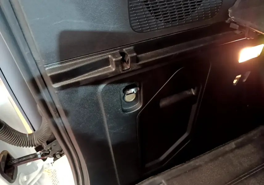 Détail intérieur du coffre noir du Renault Kangoo blanc, avec prise 12V et éclairage latéral allumé.