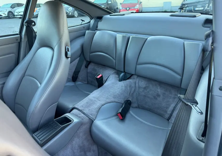 Vue intérieure arrière de la Porsche 911 Carrera 2 gris polaire de 1996, montrant les sièges en cuir gris et les ceintures de sécurité.