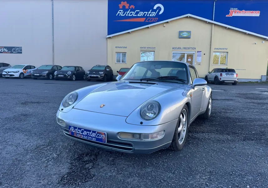 Porsche 911 Carrera 993 gris polaire vue 3/4 avant droit, avec phares ronds caractéristiques et jantes alliage 17 pouces.