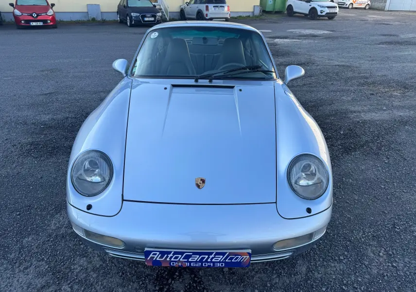 Vue avant d'une Porsche 911 Carrera 2 type 993 gris polaire, avec phares ronds caractéristiques et pare-brise teinté dégradé.