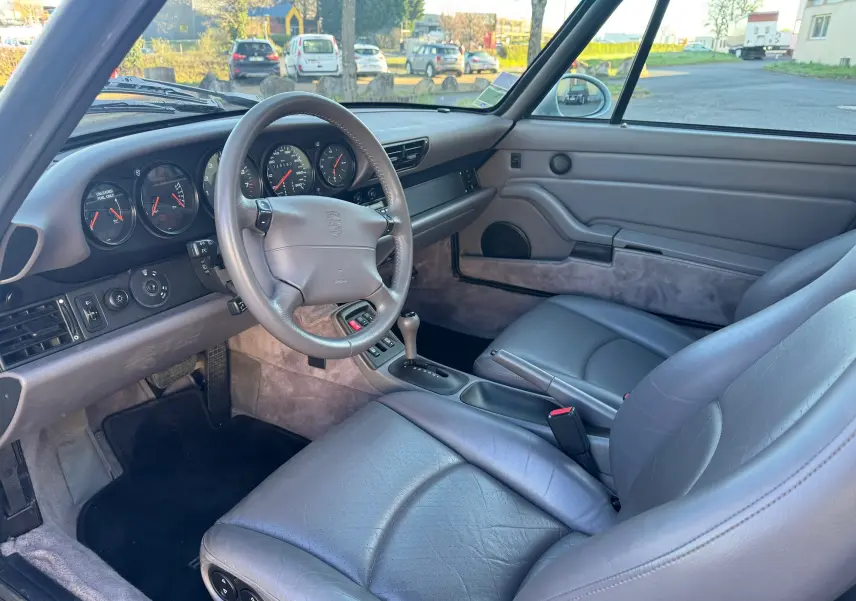 Intérieur gris de la Porsche 911 Carrera 993 vue côté conducteur, avec volant cuir et tableau de bord classique.