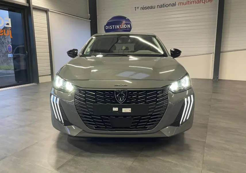 Peugeot 208 gris Selenium vue de face en intérieur, avec calandre noire et feux LED allumés.