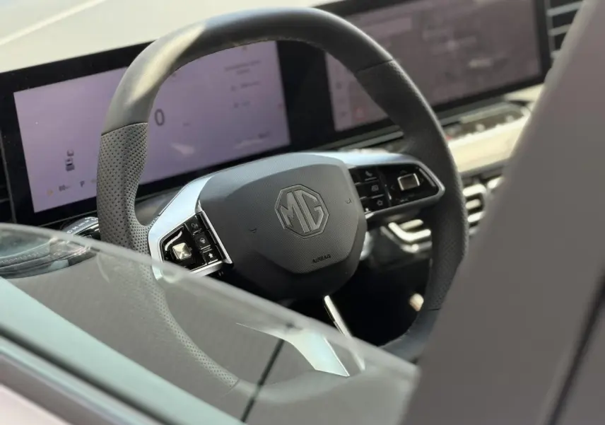 Vue rapprochée du volant noir perforé MG EHS 1.5 Hybrid+ 224 Luxury avec tableau de bord numérique en arrière-plan.