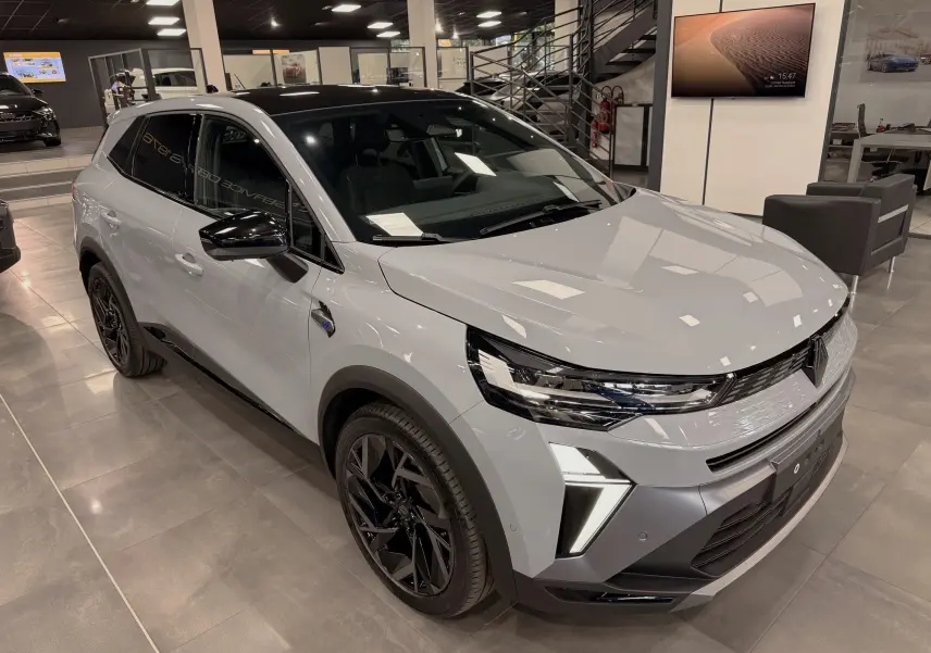 Renault Symbioz E-Tech gris Rafale en 3/4 avant droit, avec jantes noires et feux LED distinctifs, en showroom intérieur.