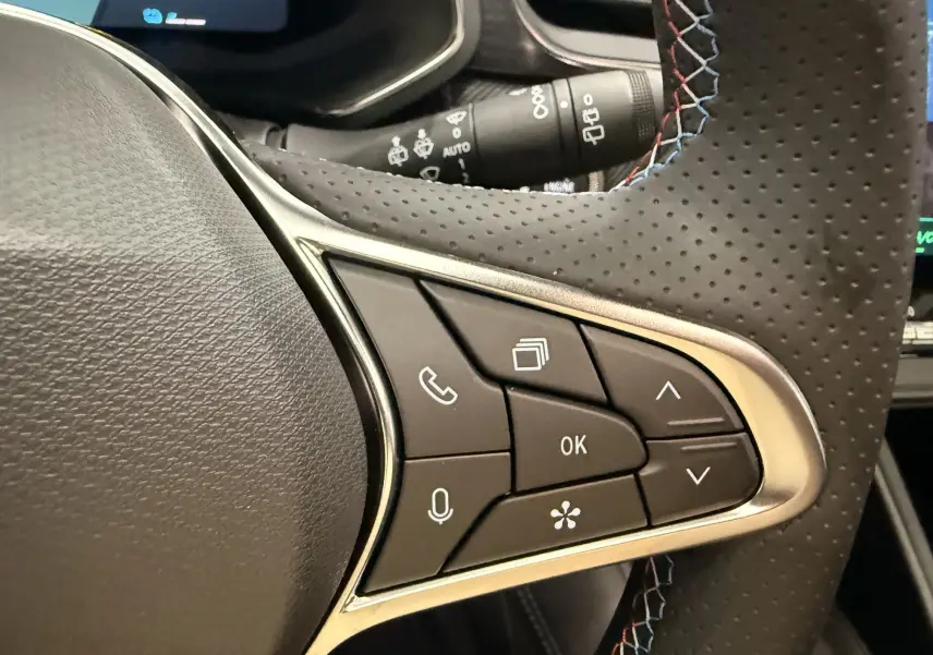 Gros plan sur le volant en cuir perforé avec surpiqûres tricolores du Renault Symbioz gris, boutons de commande multifonctions visibles.