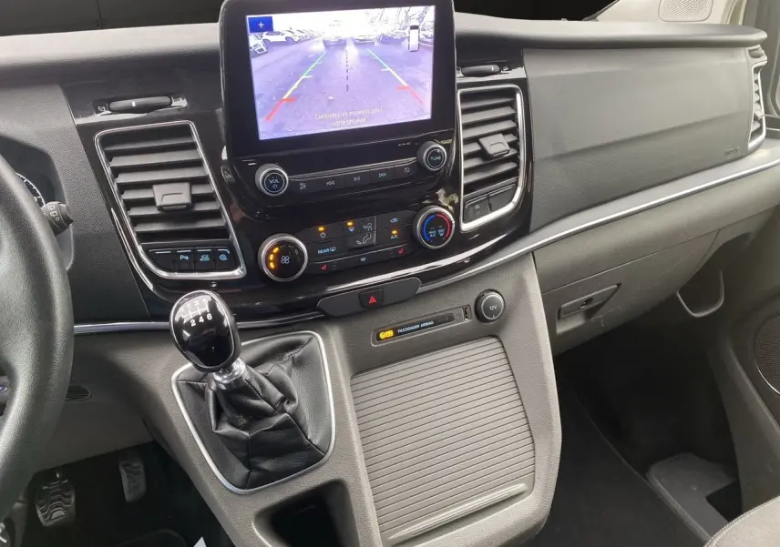 Vue intérieure du tableau de bord du Ford Tourneo Custom gris, avec écran tactile et levier de vitesses manuel visible.