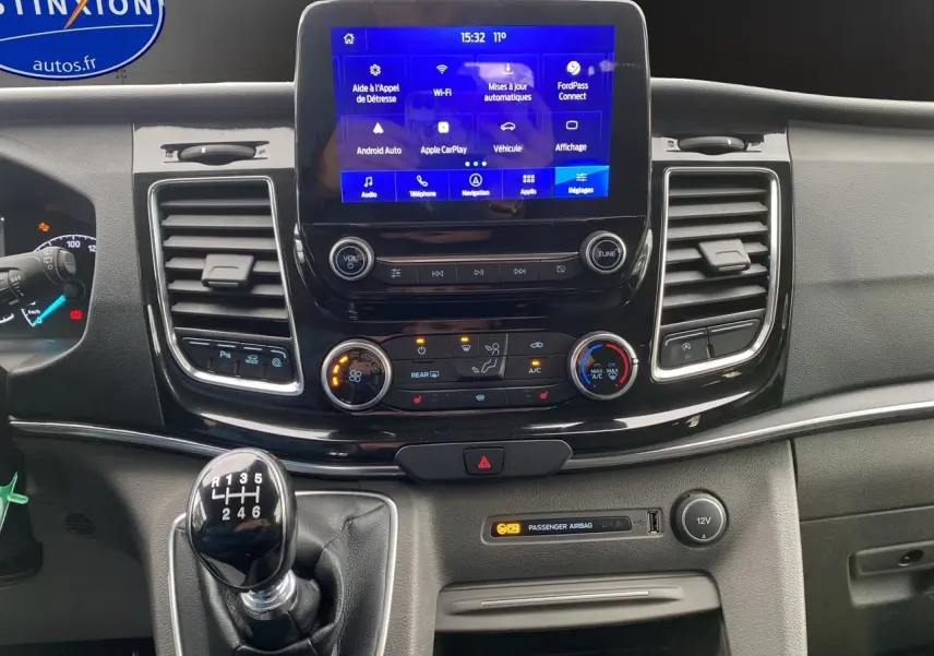 Vue rapprochée du tableau de bord du Ford Tourneo Custom gris, avec écran tactile et levier de vitesses manuel visible.