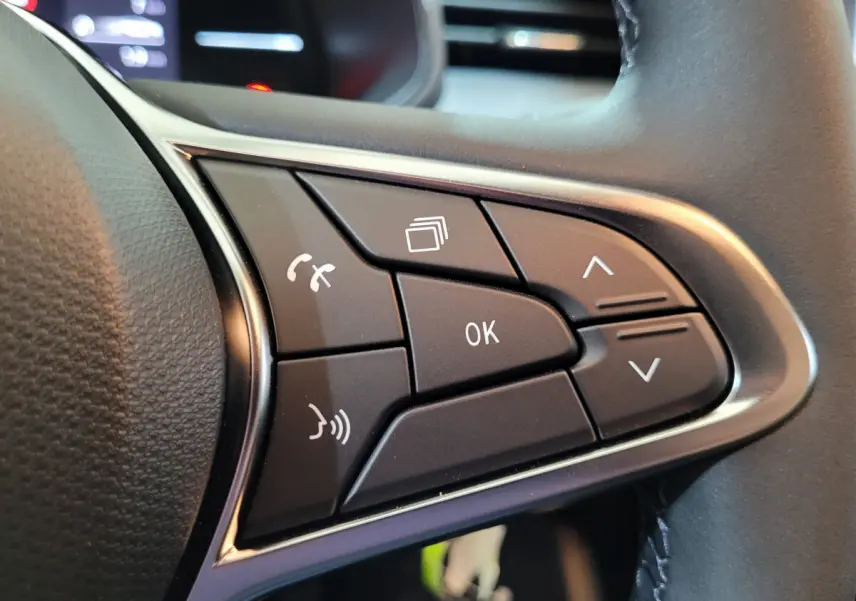 Gros plan sur les commandes multifonctions noires du volant cuir synthétique d’une Renault Clio gris foncé 2025.