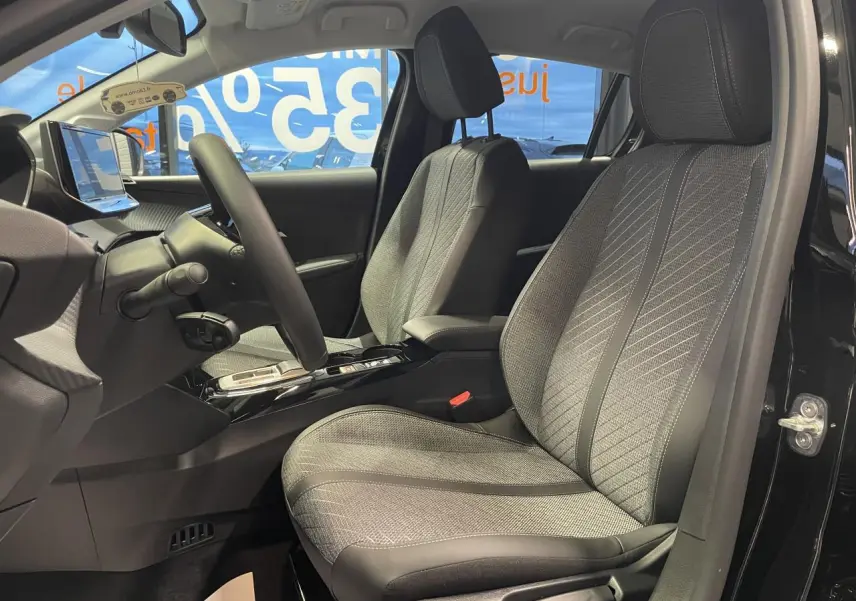 Vue intérieure côté conducteur de la Peugeot 208 noire métallisée, sièges tissu gris à motifs et volant compact cuir.