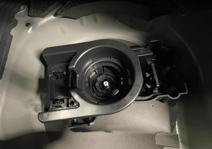 Gros plan sur le rangement de roue de secours dans le coffre d'une Peugeot 208 noire métallisée, sans roue visible.