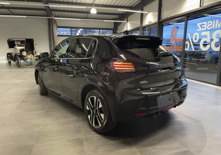 Vue 3/4 arrière droite d'une Peugeot 208 noire métallisée avec feux arrière LED et jantes alliage bi-tons dans un showroom.