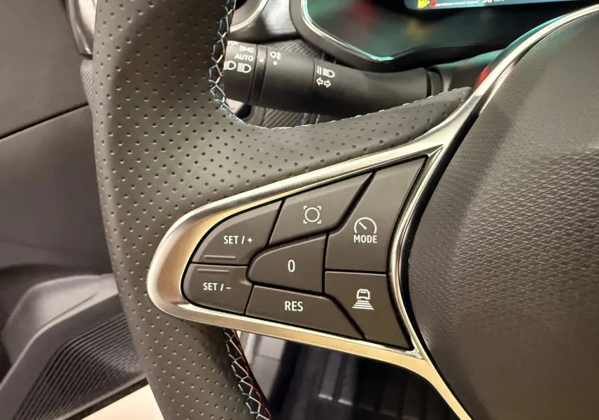 Gros plan sur les commandes gauche du volant perforé noir du Renault SYMBIOZ gris Rafale, avec boutons de régulateur et mode conduite.
